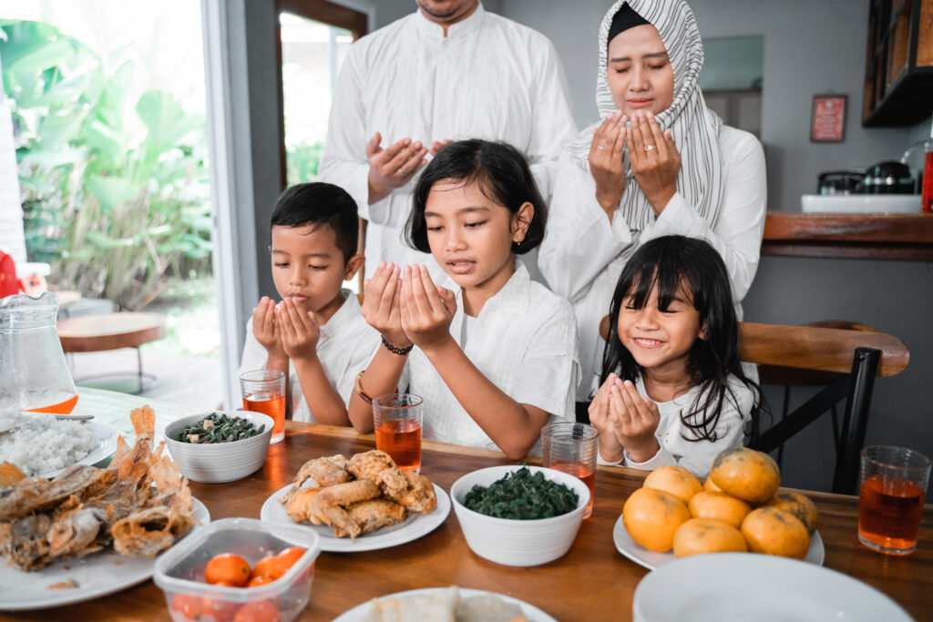 Muslim family praying before eating their food. breaking the fast or iftar dinner.