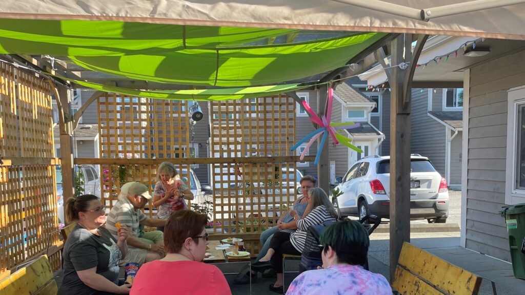 A group of Granville Garden Co-op members sitting in an outdoor cooling area under green shade sails.