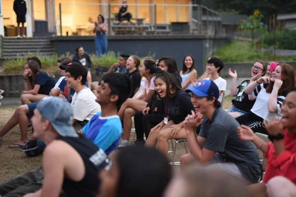 a group of campers sitting on a field laughing.