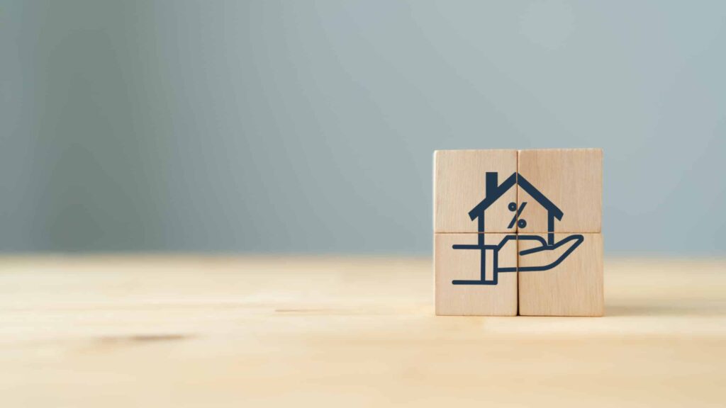 Home loan, mortgage and buy a real estate concept. The wooden cube with icon of hands holding house model in grey background and copy space. Banner for home buying, loan and insurance. financial services.