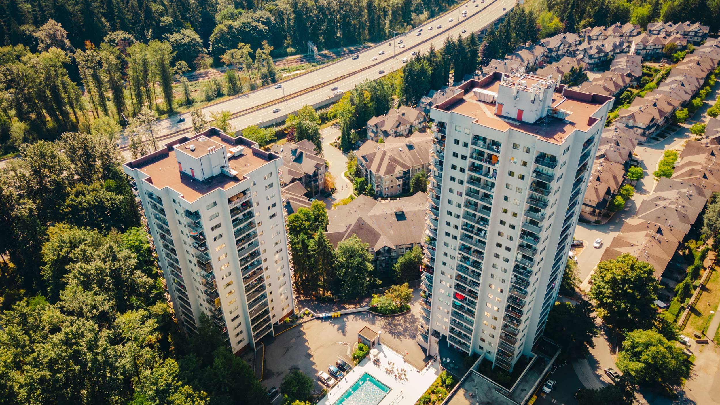 Aerial view of two high-rise apartment towers among trees beside a highway