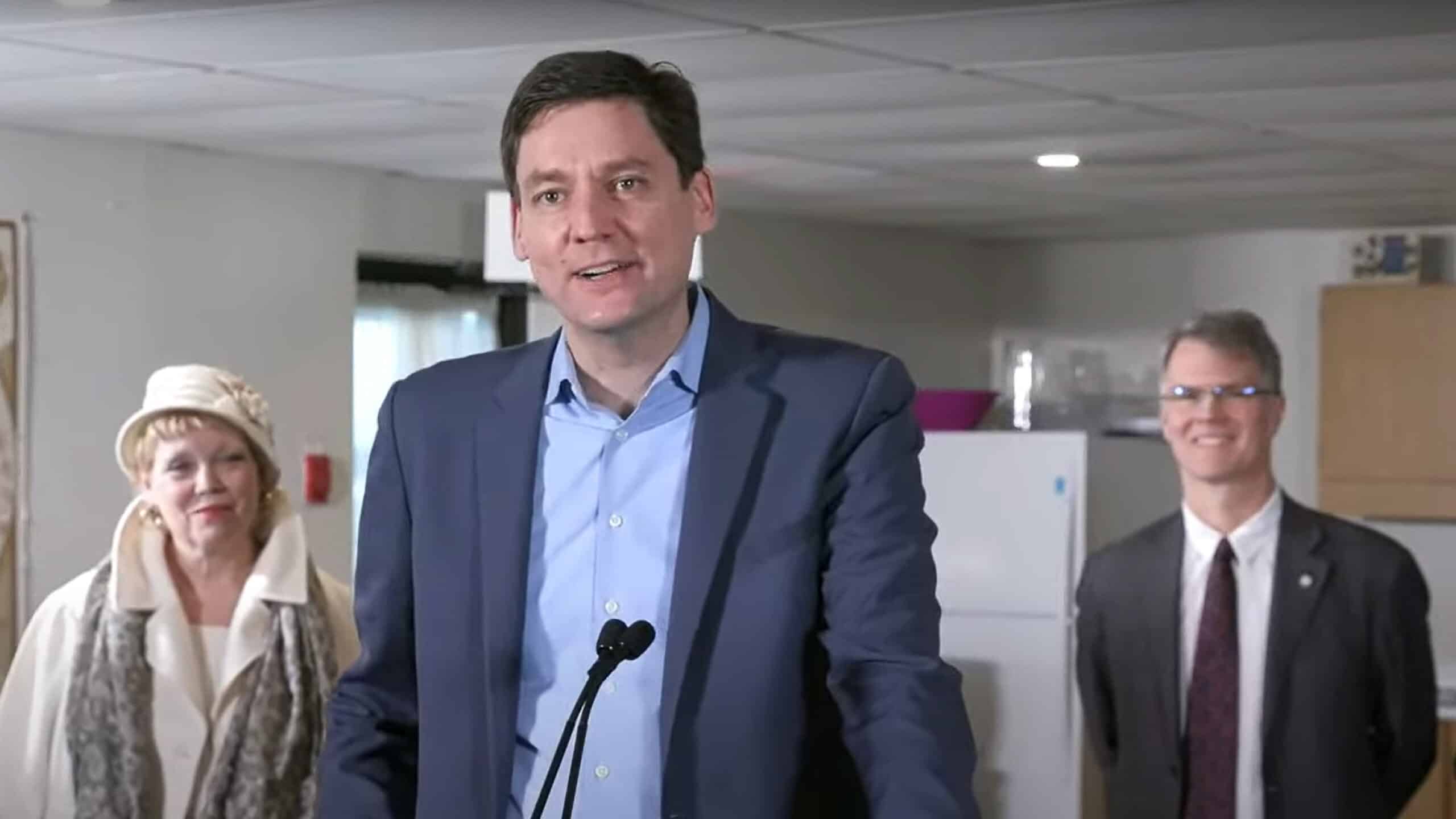 Premier David Eby speaking at a podium with two people standing behind him