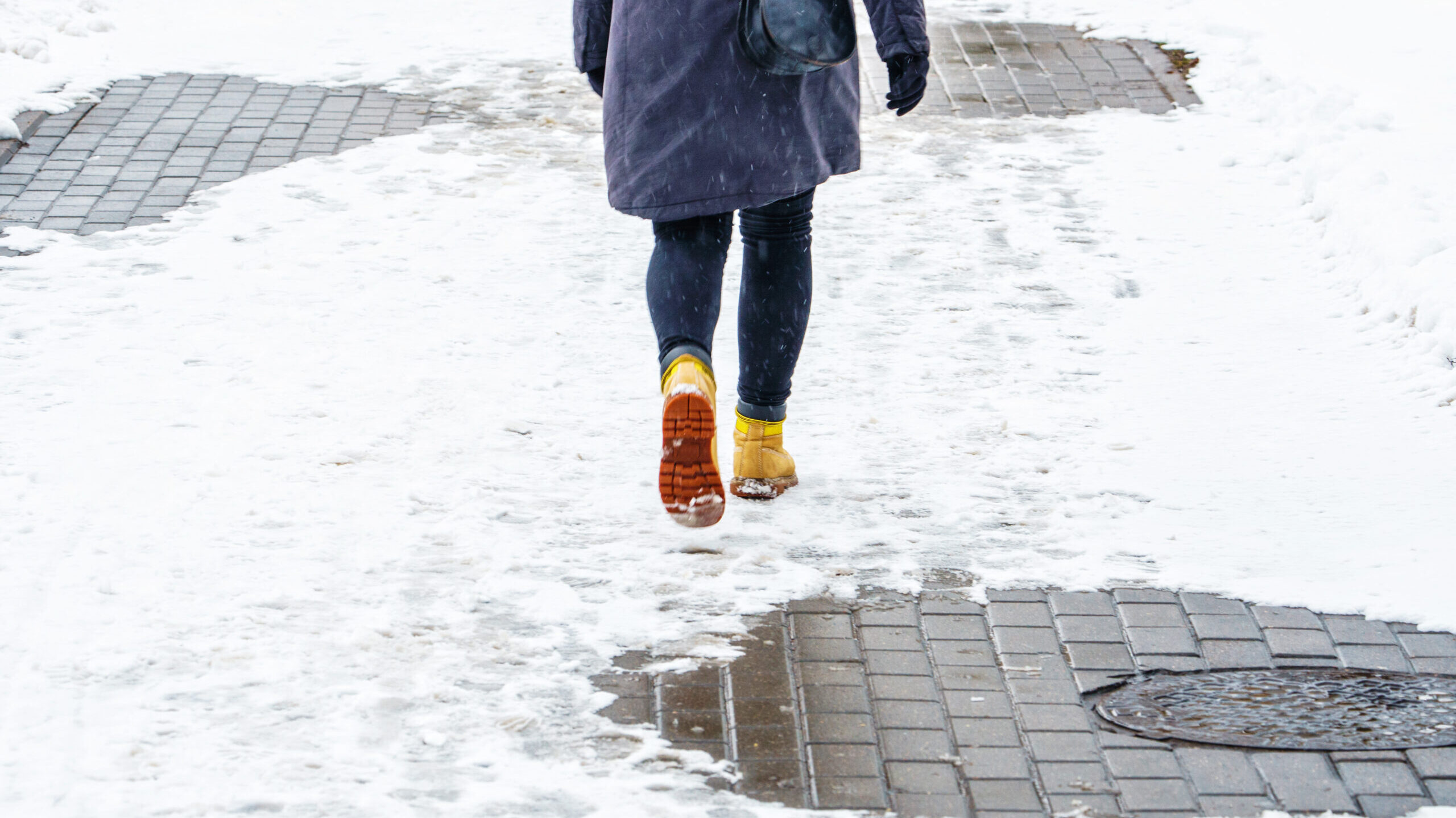 Person in yellow boots walking along a snowy sidewalk