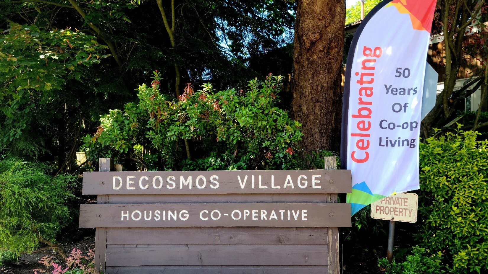 DeCosmos Village Housing Co-operative entrance sign with a "Celebrating 50 Years of Co-op Living" flag