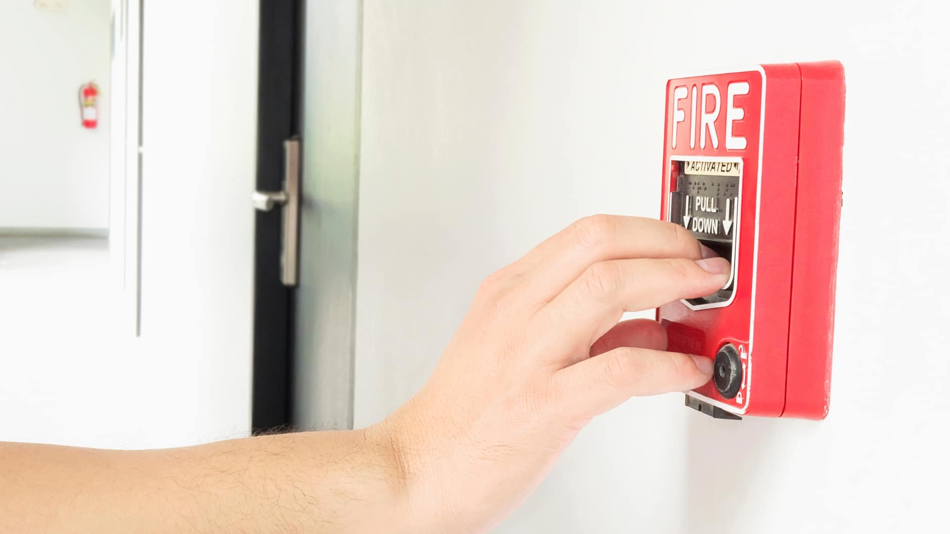 Person pulling a red wall-mounted fire alarm