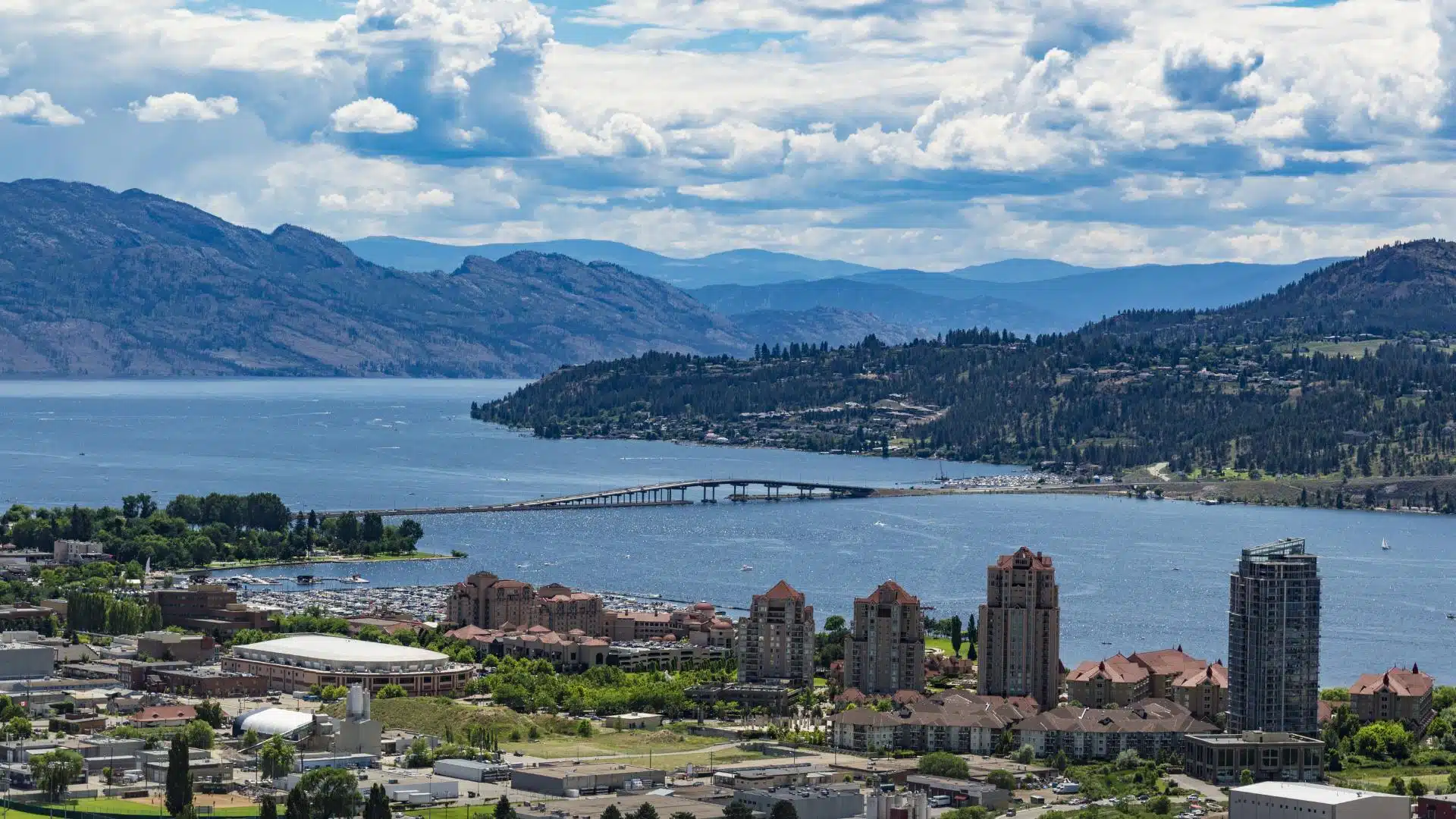 Aerial view of Kelowna's waterfront, a bridge, and towers along Okanagan Lake