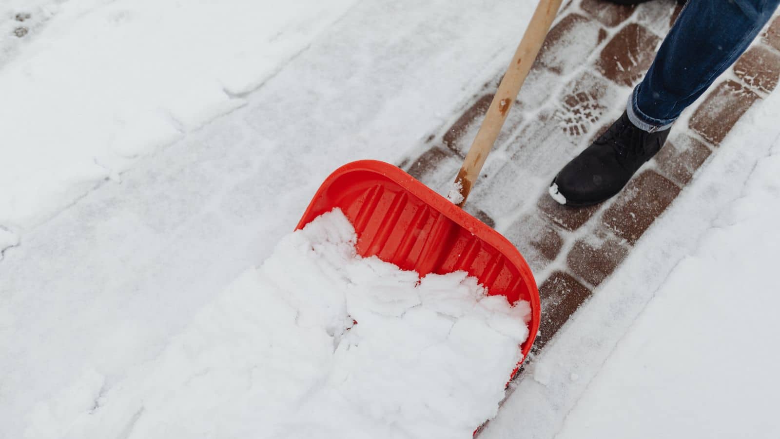 Person clearing snow from a brick walkway with a red shovel