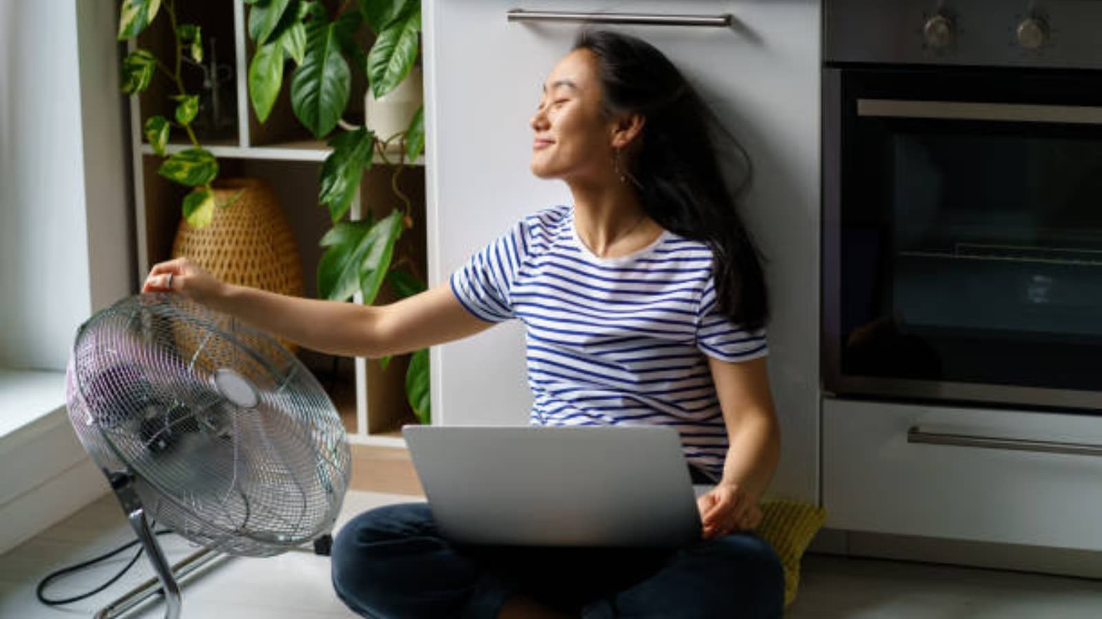 Woman cooling off beside a fan while working on a laptop in summer
