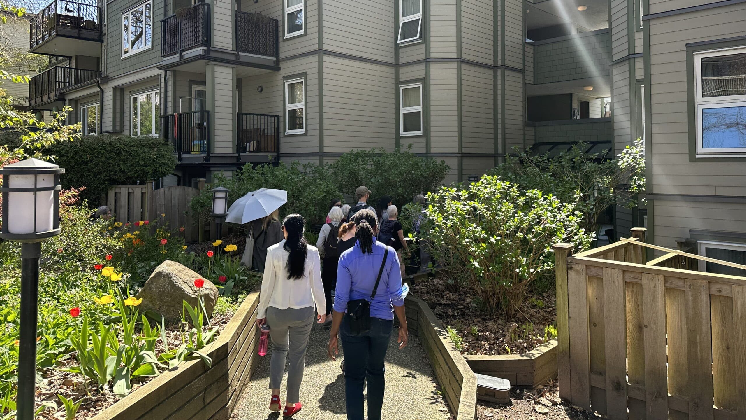 Group touring a co-op courtyard with garden beds and tulips beside a low-rise building